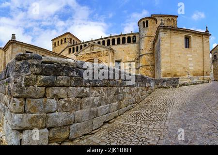 Panoramic of old stone Romanesque church with cobblestone pavement and blue sky. Santillana del Mar. Stock Photo