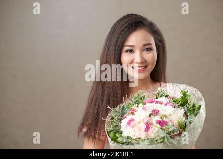Smiling Asian woman holding bunch of flowers Stock Photo