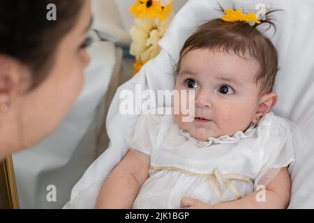 beautiful dark eyed latina baby lying on her crib looking at her mother. young mother spoiling her six month old baby girl. concept of motherhood and Stock Photo