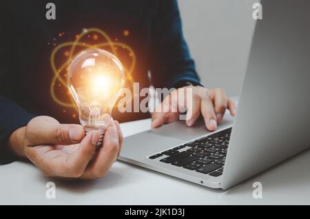 Hand man holding bulb light idea creativity inspiration and using computer laptop on desk. Stock Photo