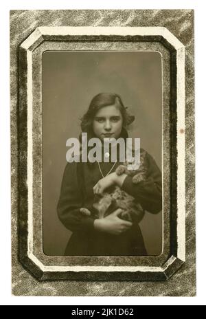 Original Edwardian era postcard portrait of pretty girl of teenage years with long hair, holding her pet kitten. The postcard has a mock frame. Written on reverse is  'with every good wish from all at 24 Charleville Road',  dated Xmas 1911 London or Birmingham - England, U.K. Stock Photo