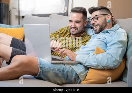 Male caucasian gay couple using laptop computer at home. High quality photography. Stock Photo
