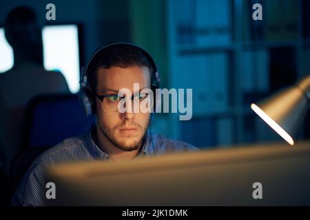 Software developer listening to music and working on computer late at night Stock Photo