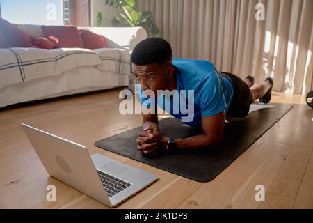 Young African American black male athlete watching workout videos on his laptop doing an online class while holding plank position. Keeping fit Stock Photo