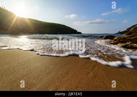 Sea wave approaching the beach with glimpses of the sun setting behind a mountain. Santander. Stock Photo