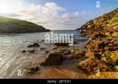 Rocky beach in clear water and glimpses of the sun setting behind the mountain. Santander. Stock Photo