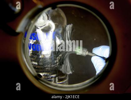 A forensic technician examines fingerprints on a liquor bottle from a crime scene. Stock Photo