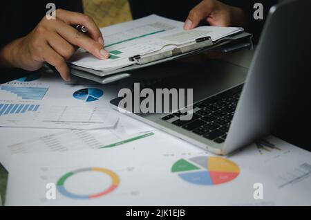 Businessman person pointing document graph financial marketing report and paperwork chart analysis investment with computer laptop on desk at office. Stock Photo