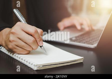 person man holding pen write plan or idea on book with computer laptop on desk. Stock Photo