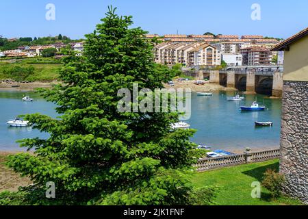 Estuary of the sea under the bridge with small boats anchored and large green tree. Stock Photo