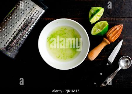 Making Lime Cordial on a Wood Tabletop: Mixing simple syrup with lime juice and zest to make a cocktail mixer Stock Photo