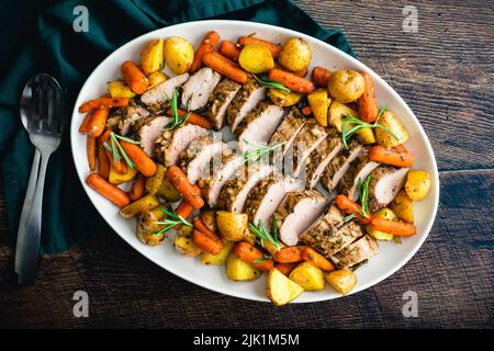 Roast Pork Tenderloin with Potatoes and Baby Carrots: Sliced pork medallions surrounded with vegetables on a platter Stock Photo