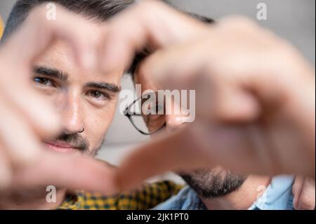 Young gay couple smiling confident doing heart symbol with hands at home. High quality photography. Stock Photo