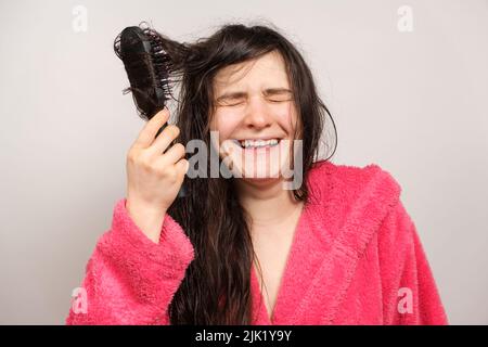 A woman in a pink robe combs her wet hair with a comb and laughs Stock Photo