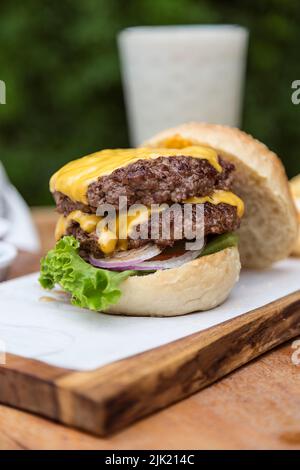 double cheeseburger with onions, tomato, lettuce and cheddar cheese on a wooden board Stock Photo