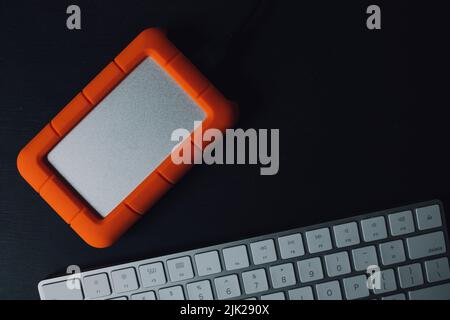 orange External hard drive on black desk with silver white keyboard Stock Photo