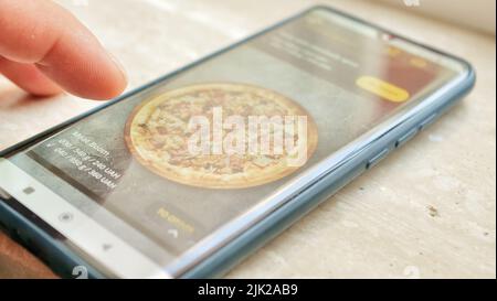 The Process of Selecting and Ordering Takeaway Food Pizza Online in the Mobile App Using a Phone. Close-up of the Smartphone Screen and Male Fingers Stock Photo