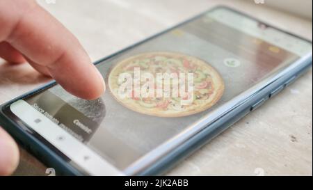 The Process of Selecting and Ordering Takeaway Food Pizza Online in the Mobile App Using a Phone. Close-up of the Smartphone Screen and Male Fingers Stock Photo