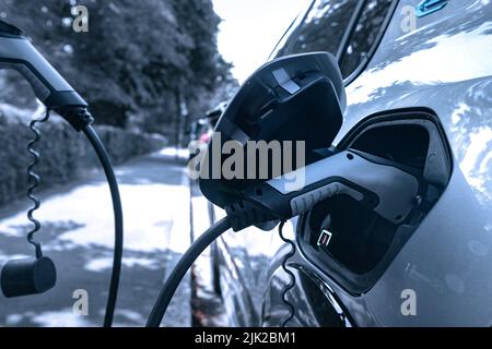 Electric car plugged in and changing on urban city street Stock Photo
