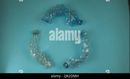 Three crashed plastic bottles on blue background form resycling sign. Plastic utilisation concept. Attractive ecological problem positive poster Stock Photo