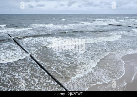 Seaside of Baltic Sea in Poland. Stormy sea, with waves hiting wooden poles. Bird view, aerial view from high up. Stock Photo