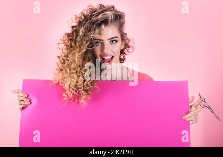 Curly hair girl with advertising board and scissors. Hairdresser. Beauty salon. Makeup and cosmetic. Stock Photo