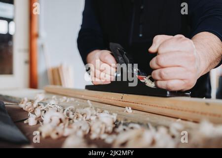 unrecognizable man using old steel carpenter brush carving a wooden stick, in his workshop. Selective focus Stock Photo