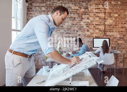 Architect, design engineer or building contractor drawing a plan on a drafting table for a project or development in his office. A male designer doing Stock Photo