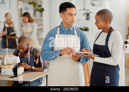 Entrepreneurs planning and discussing booking for sewing lessons on a digital tablet in the classroom. Sewing teacher and assistant talking about Stock Photo