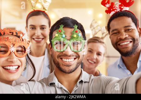 We worked hard all year, now to enjoy a little break. Portrait of a group of businesspeople taking selfies together during a Christmas party at work. Stock Photo