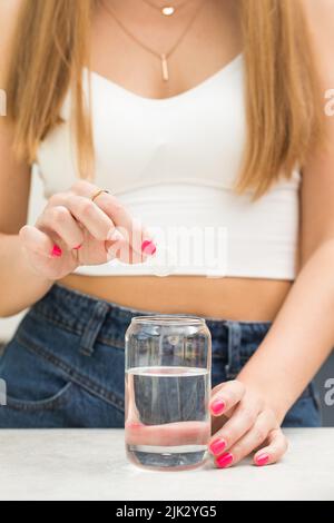A woman throws a white round pill into a glass of water. Pain reliever, complex vitamins for women's health. Stock Photo