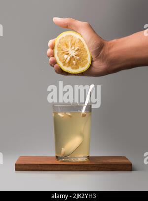 hand squeezing orange fruit into a glass of juice with a spoon on a wooden tray, isolated on gray background Stock Photo