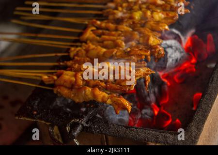 sate ayam or chicken satay , or chicken or meat satay with charcoal  ingredient on red fire grilling by people. traditional satay from, Indonesia Stock Photo