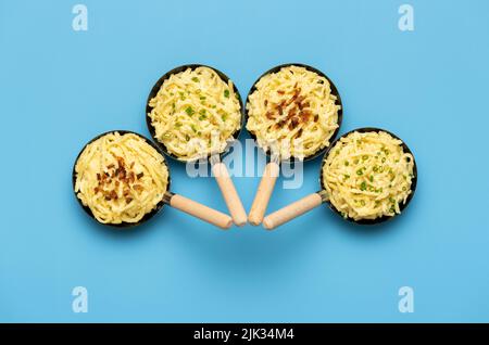 German noodles topped with chives and roasted onion, in small iron pans on a blue table. A bavarian traditional dish, pasta with cheese Stock Photo