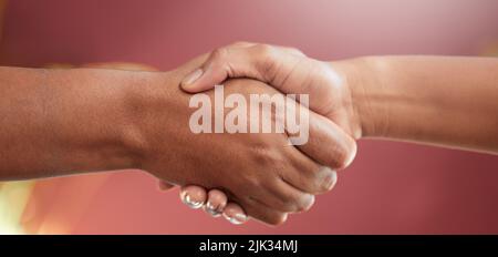 Its a done deal. two unrecognizable people shaking hands in studio against a red background. Stock Photo