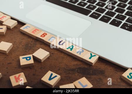 February - colourful wooden square letters on a dark wooden table next to a silver laptop with black keyboard. High quality photo Stock Photo