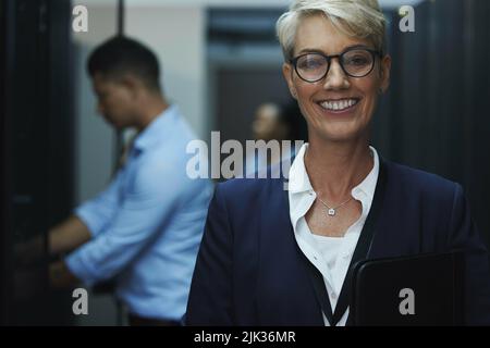 Youll see me when you request their leader. Portrait of a cheerful mature woman working in a server room. Stock Photo