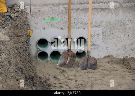 2 shovels stand on a wall with openings for cables Stock Photo
