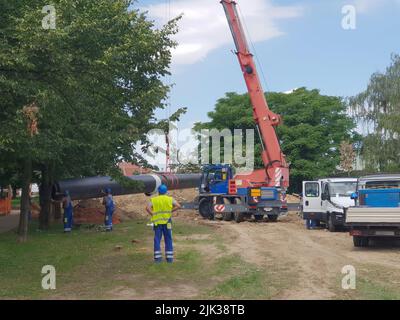 Laying heating pipes in a trench at construction site. Reconstruction site of district heating system pipeline and replacement of old pipes with new o Stock Photo