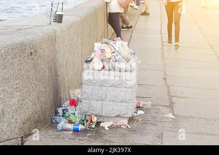 Sunset, an overflowing trash bin and scattered garbage on the embankment. Stock Photo