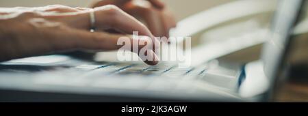 Low angle closeup view of female hands typing on laptop computer keyboard with focus on the hand in front and blurred background. Stock Photo