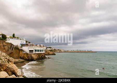 A couple swimming at the mediterranean sea in the rocky coasts near San Sebastian beach at Sitges, Barcelona Province. Sitges port at the bottom Stock Photo