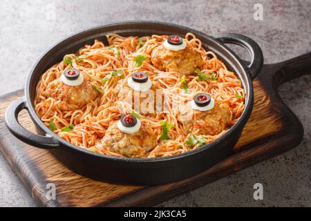 Halloween dinner of meatballs with monster eyes and pasta with tomato sauce in a frying pan on the table close-up. Horizontal Stock Photo