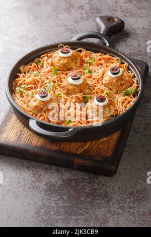 Spaghetti with tomato sauce and meatballs with funny eyes on the table close-up. Funny decorations. Halloween Food. Vertical Stock Photo