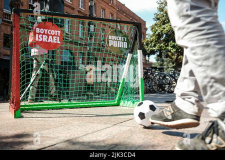 Toulouse, France. 30th July, 2022. A boy shoots at the football goal, with 'Boycott Israel' and 'Boycott Puma' signs. At the call of the Collectif Palestine Vaincra, rehabilitated by the Council of State a few weeks ago, several activists organized an information stand for the boycott of the Champions Trophy (Trophée des Champions), and more broadly of Israeli products. The Champions Trophy is a football match between PSG (champion of Ligue 1) and FC Nantes (winner of the Coupe de France) on July 31, 2022 in Tel Aviv (Israel). For the Collective, this trophy is a commercial operation organized Stock Photo