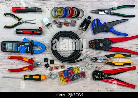Professional electrician tools and electrical components on light wooden boards. Pliers, strippers, crimpers, multimeter, tester, screwdriver. Coil of Stock Photo