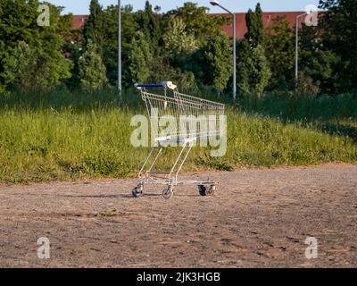 Empty shopping cart standing in the nature next to a residential area. A steel frame and grids with wheels to transport groceries. Leftover cart. Stock Photo