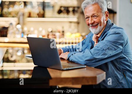 The happy senior student is sitting at his home and studying for an exam. Senior using the laptop for studying. Stock Photo