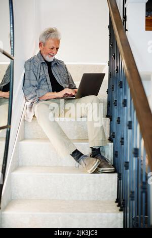 A happy senior student sits on the stairs at home with a laptop in his lap and using the it. He is checking on exam results online. Stock Photo