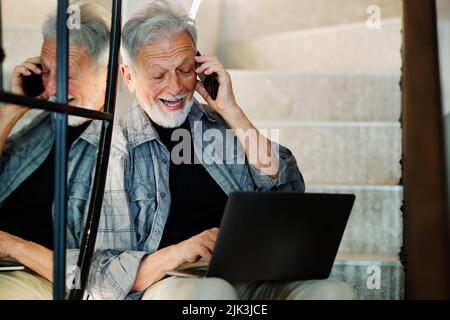A busy man on the stairs talking on the phone and typing on the laptop. Stock Photo